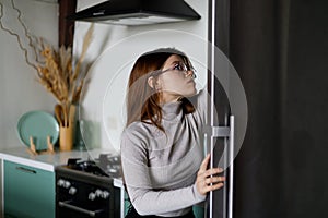 A woman after work chooses food in a black refrigerator in the kitchen, diet