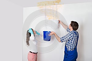 Woman With Worker Collecting Water From Ceiling In Bucket photo