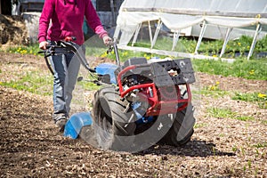 Woman worker driving rototiller tractor unit preparing soil on o photo