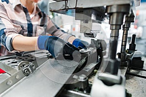 Woman worker in factory producing parts on punching machine