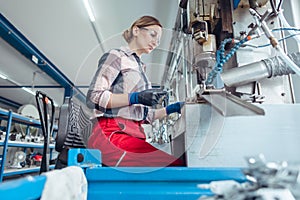 Woman worker in factory producing parts on punching machine