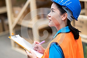The woman worker holds clip charts and takes notes in the automotive parts warehouse store. Engineers wear a safety helmet, vest