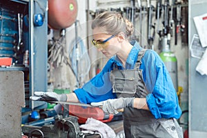 Woman worker in metal workshop deburring workpiece