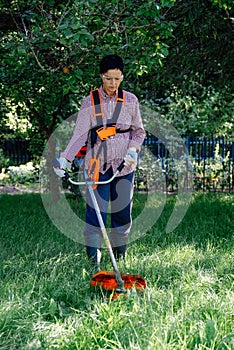 Woman worker mowing the grass in garden using string trimmer