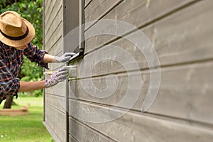 Woman worker painting wooden house exterior wall with paintbrush and wood protective color