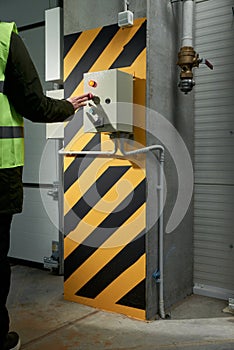 A woman worker presses the button to open the roller shutter doors at an industrial enterprise