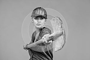 woman worker in protective helmet and boilersuit hold shovel on orange background, industry