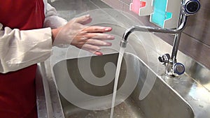 Woman worker in red apron disinfects her hands under the tap.