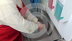 Woman worker in red apron washes her hands under the tap.