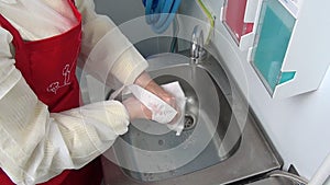 Woman worker in red apron washes her hands under the tap.