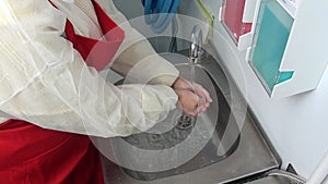 Woman worker in red apron washes her hands under the tap.