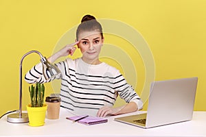 Woman worker showing stupid gesture with finger looking at camera with displeased tired expression