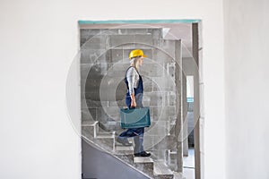 Woman worker with a tool box walking down the stairs on the construction site.