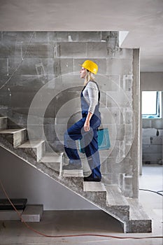 Woman worker with a tool box walking up the stairs on the construction site.