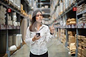 Woman worker using smartphone to checking inventory in warehouse store