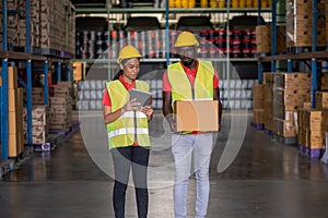 Woman worker using a tablet to check stock online and a man holding a parcel in the large warehouse distribution center. Both