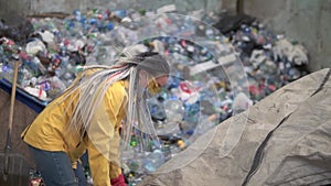 Woman-worker in yellow jacket and transparent protecting glasses sorting used plastic bottles at modern recycling plant