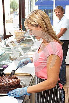 Woman Working Behind Counter In Cafe Slicing Cake