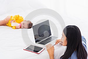 Woman is working busy on laptop computer and tablet at home while her  baby is sleeping