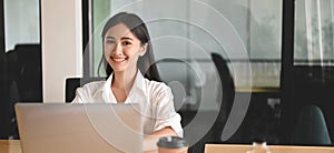 A woman is working with a computer laptop at the wooden working desk