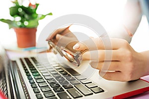 Woman working on computer in office and holding glasses