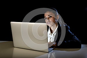 Woman working in darkness on laptop computer late at night looking stressed bored and tired