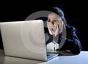 Woman working in darkness on laptop computer late at night surprised in shock and stress