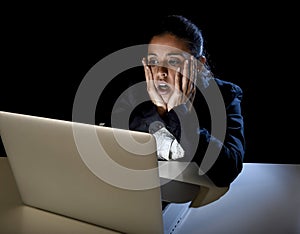 Woman working in darkness on laptop computer late at night surprised in shock and stress