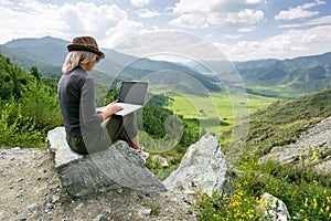 Woman working on her computer on the top of the mountain. Remote work