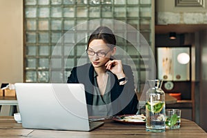 Woman working on her laptop at a cafe. Caucasian woman with glasses sitting at a cafe and working on her laptop