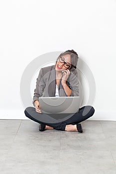 Woman working on her laptop, talking on phone sitting on floor