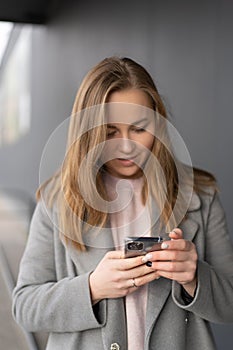 Woman working on her phone outdoors. Cold autumn weather