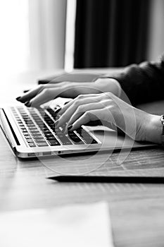 Woman working at home with laptop is typing text. Female hands on the keyboard, black and white photo.