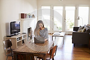 Woman Working From Home Using Laptop On Dining Table