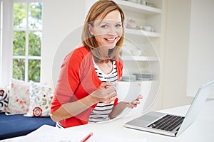 Woman Working From Home Using Laptop In Kitchen