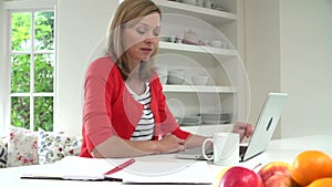 Woman Working From Home Using Laptop In Kitchen