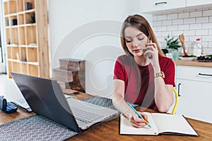 Woman working at home write notes while talking on phone photo