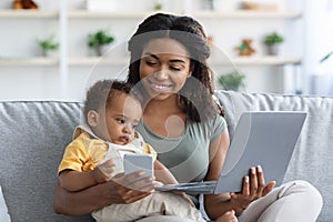 Woman working with laptop and cellphone at home with child in arms