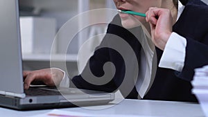 Woman working on laptop and chewing pencil, bad habit from stressful job closeup