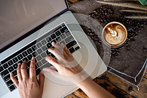 Woman working with laptop computer with latte art coffee cup and coffee beans on wood table