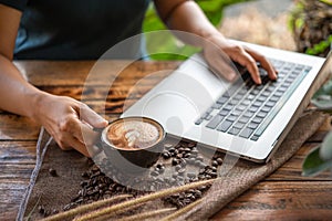 Woman working with laptop computer with latte art coffee cup and coffee beans on wood table