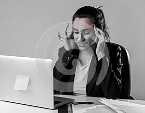 Woman working at laptop computer office desk in stress suffering intense headache and migraine