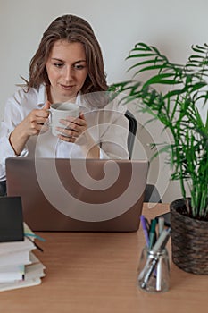 Woman working on laptop at home office while drinling coffee. Web conection