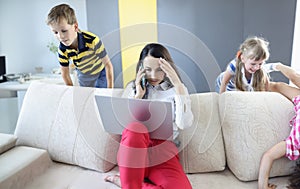 Woman working on laptop at home talking on phone and children playing