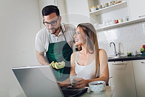 Woman working on laptop in kitchen as boyfriend prepares meal