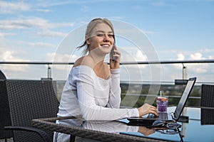 Woman working on laptop at office while talking on phone. Portrait of young smiling business woman calling her best