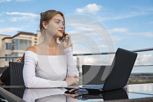Woman working on laptop at office while talking on phone. Portrait of young smiling business woman calling her best