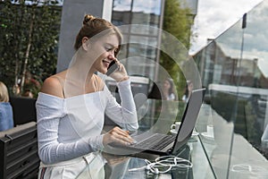 Woman working on laptop at office while talking on phone. Portrait of young smiling business woman calling her best