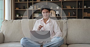 Woman working on laptop seated on sofa cross-legged at home