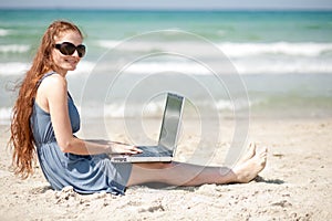 Woman working on a laptop by sitting on the beach